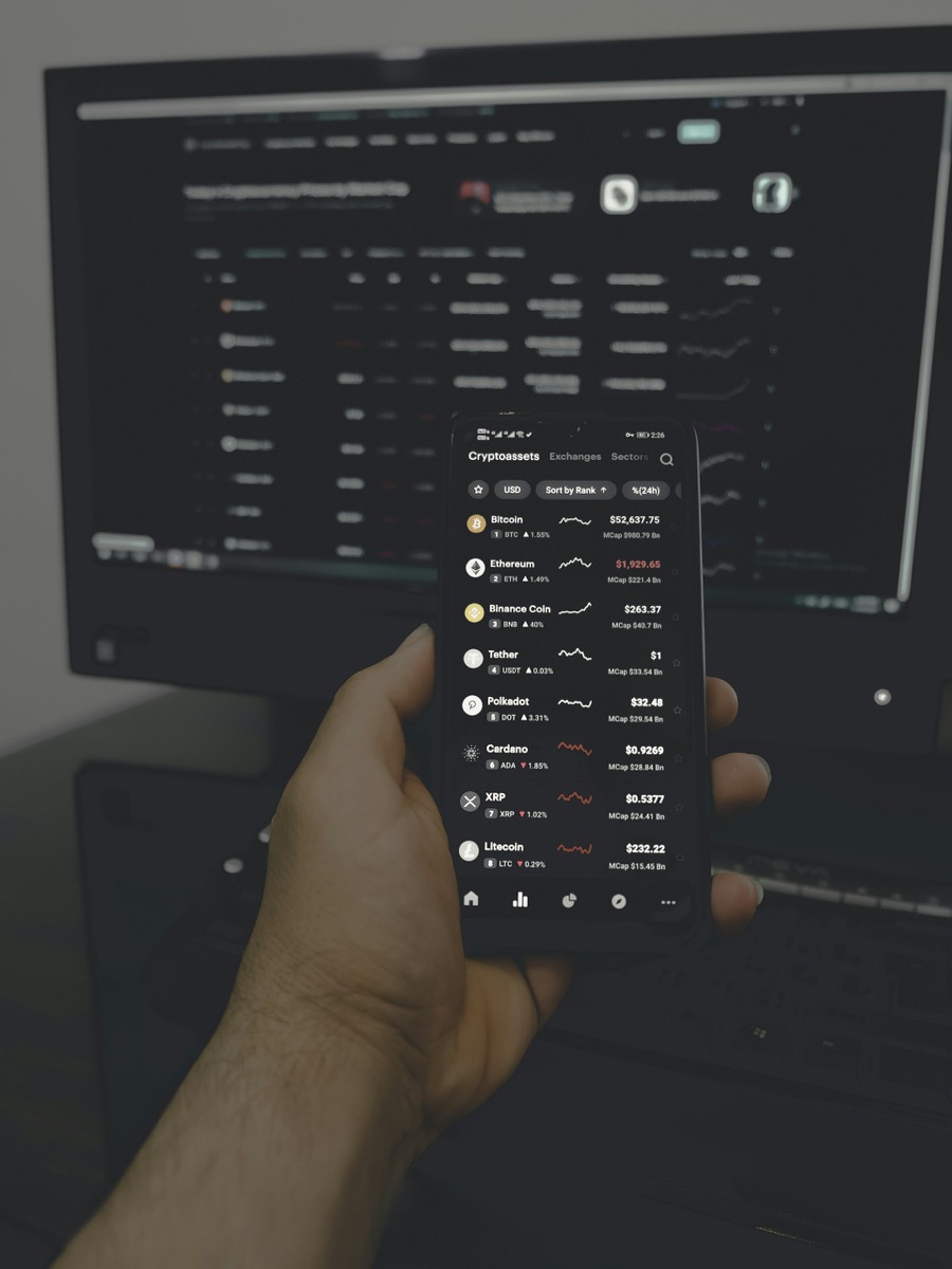 Hand holding a smartphone with a live operations dashboard in front of a monitor